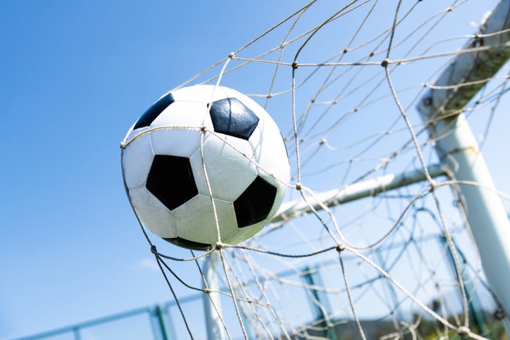 soccer ball in soccer net, ball is above ground and blue sky in the background