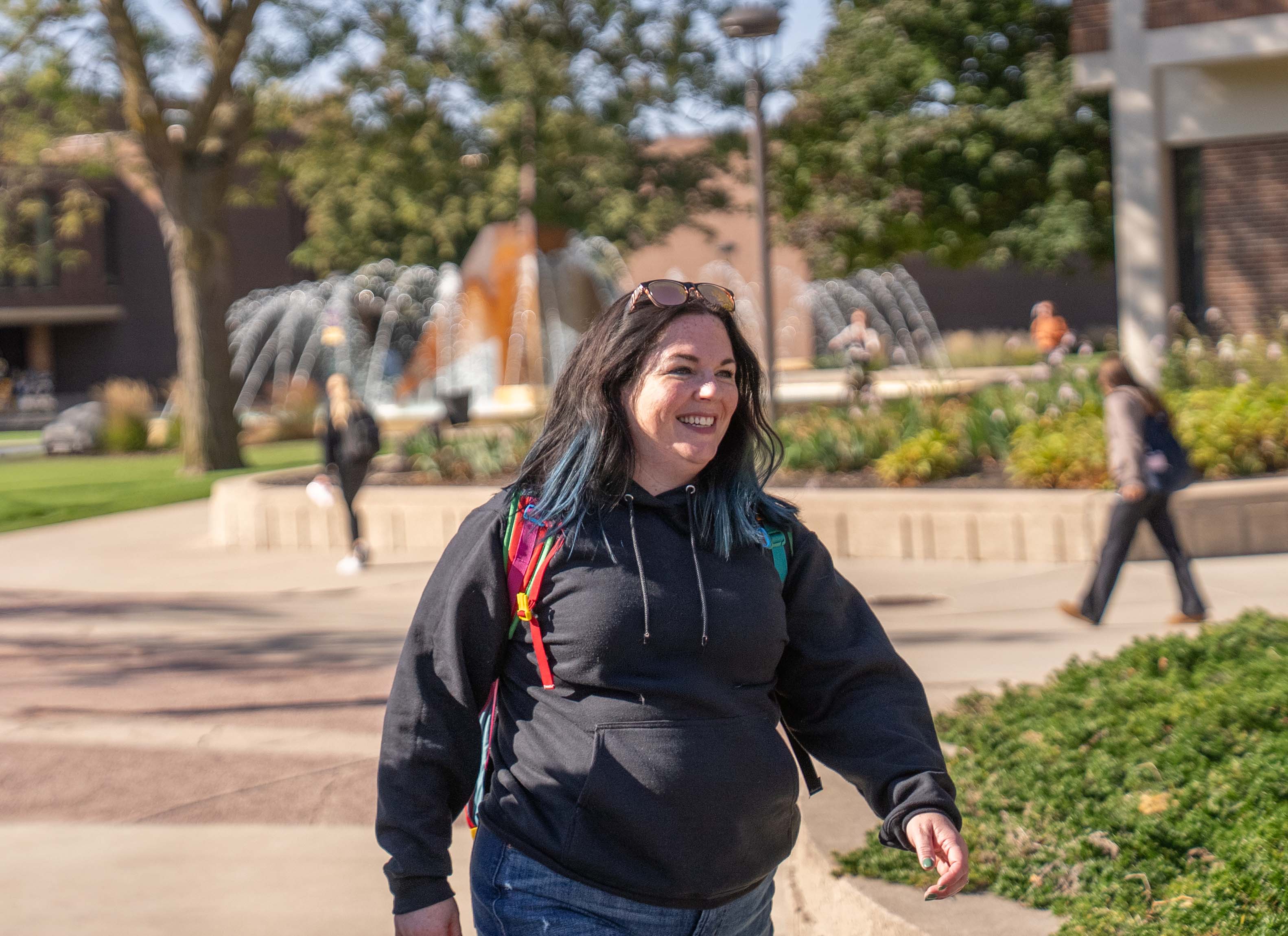 student on outside on campus wearing a black sweatshirt with brown hair and a backpack by the fountain