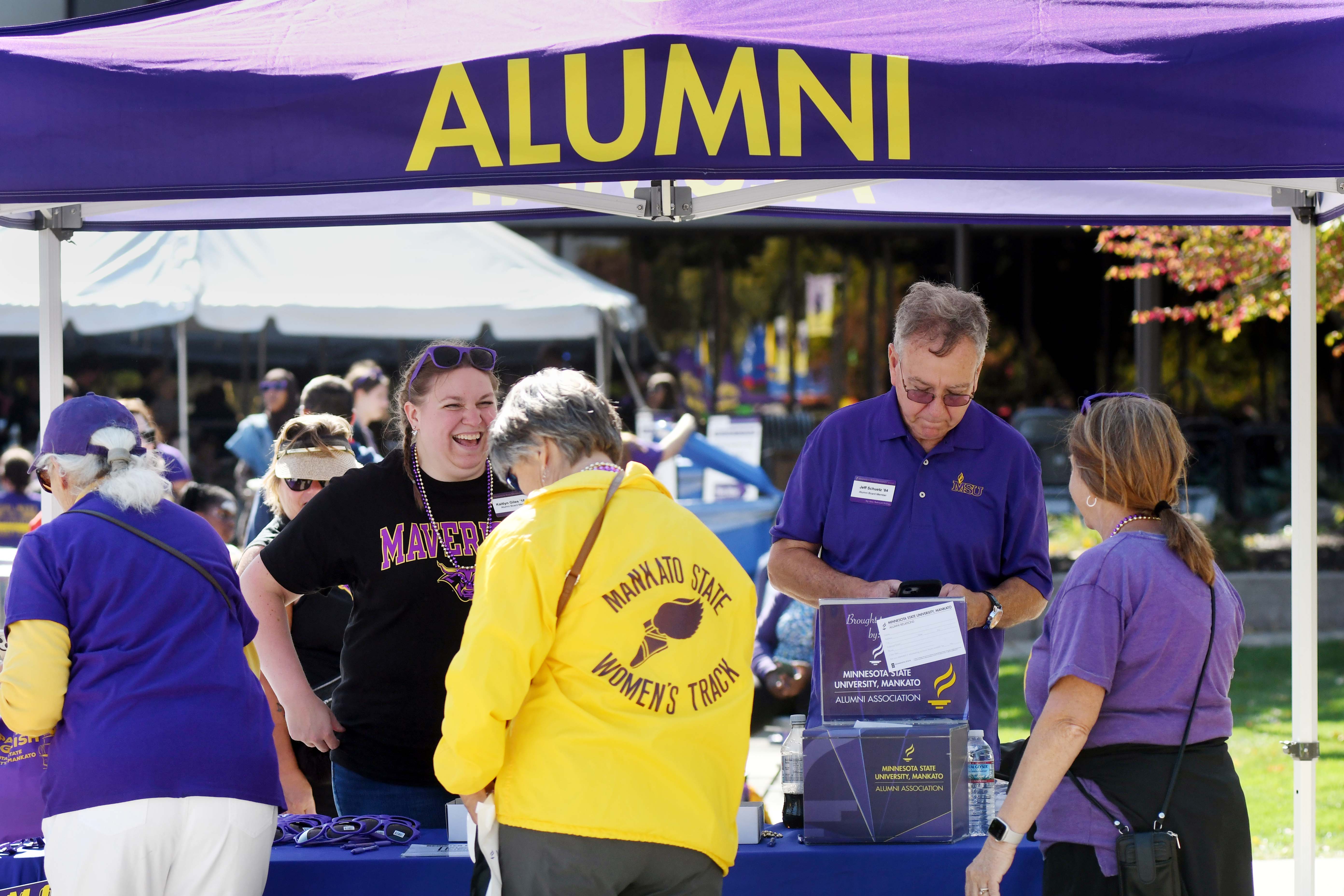 Group of people conversing under an alumni tent at an event.