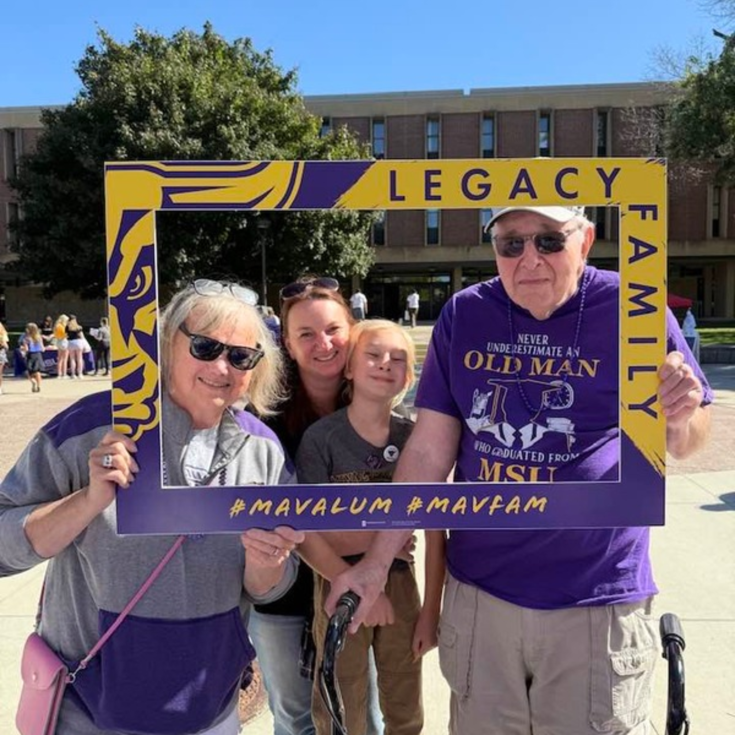 msu alumni family standing together holding a msu legacy family photo frame