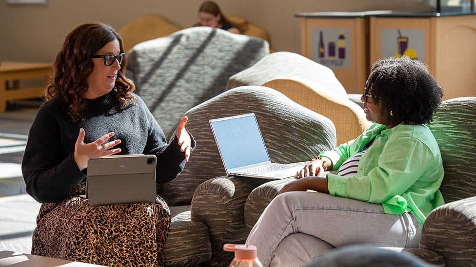 Two graduate students sitting in the Centennial Student Union talking with their laptops open