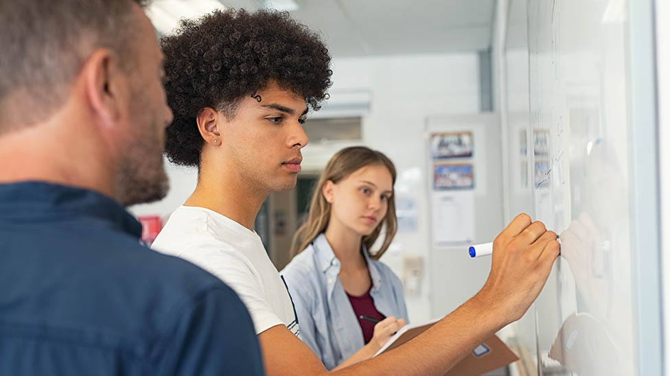 High School teacher watching two high school students calculate a math problem on the white board