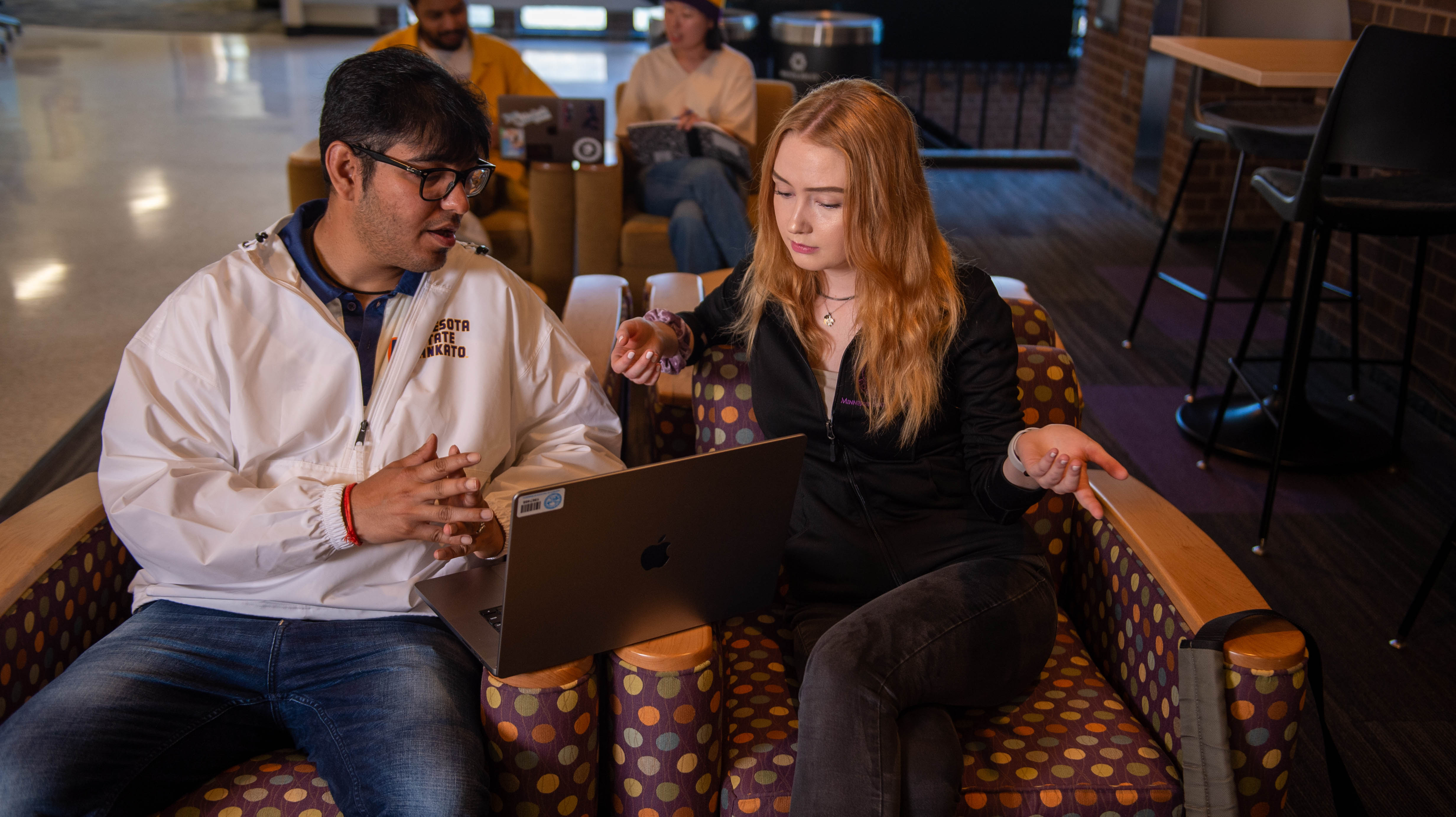 two international students sitting in front of a laptop communicating with one another