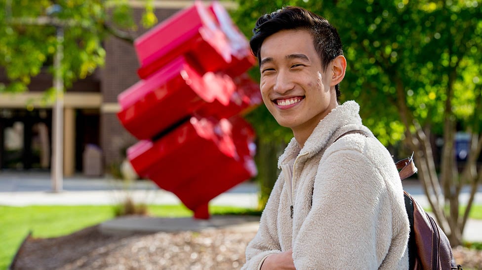 a person smiling in front of a red sculpture