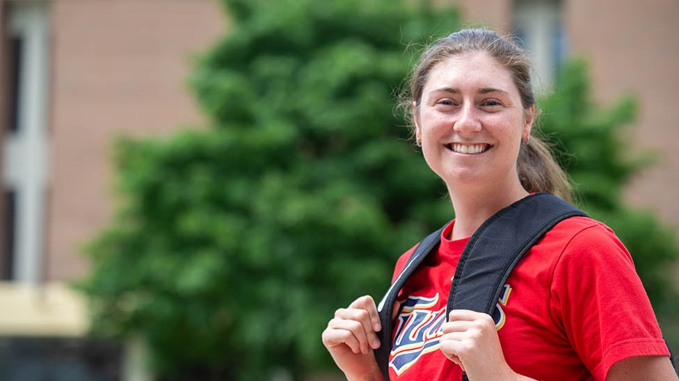 student standing outside holding a backpack smiling