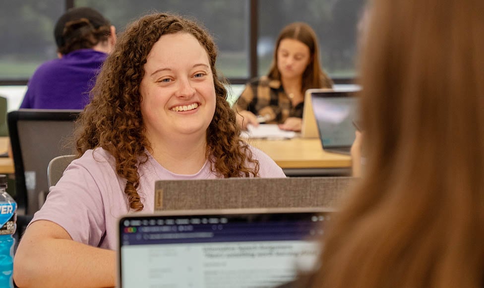 Transfer student sitting at a work table with another student and their laptops out