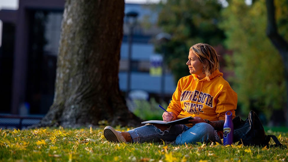Transfer student sitting outside on campus, during the fall, working on homework