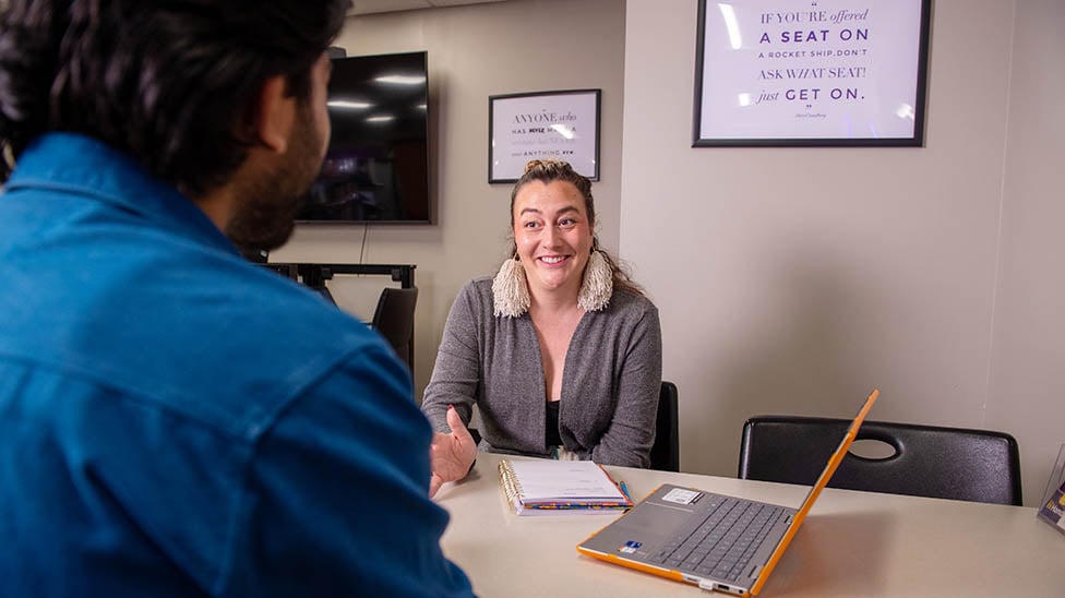 A one on one session with an advisor showing a student something on the computer and both smiling at each other