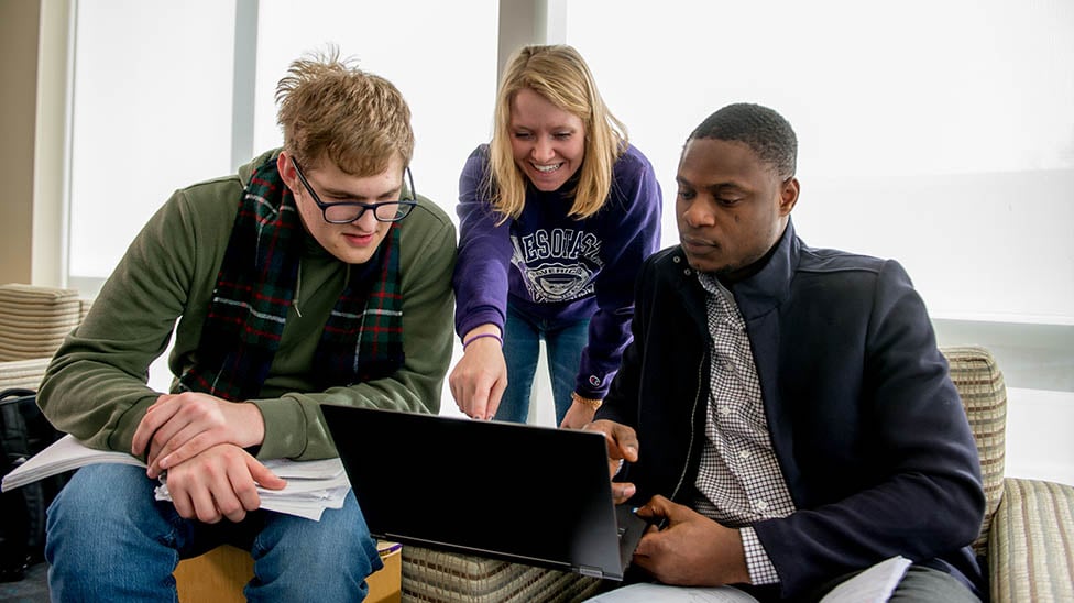 three students sitting around a computer and looking at the content on the screen