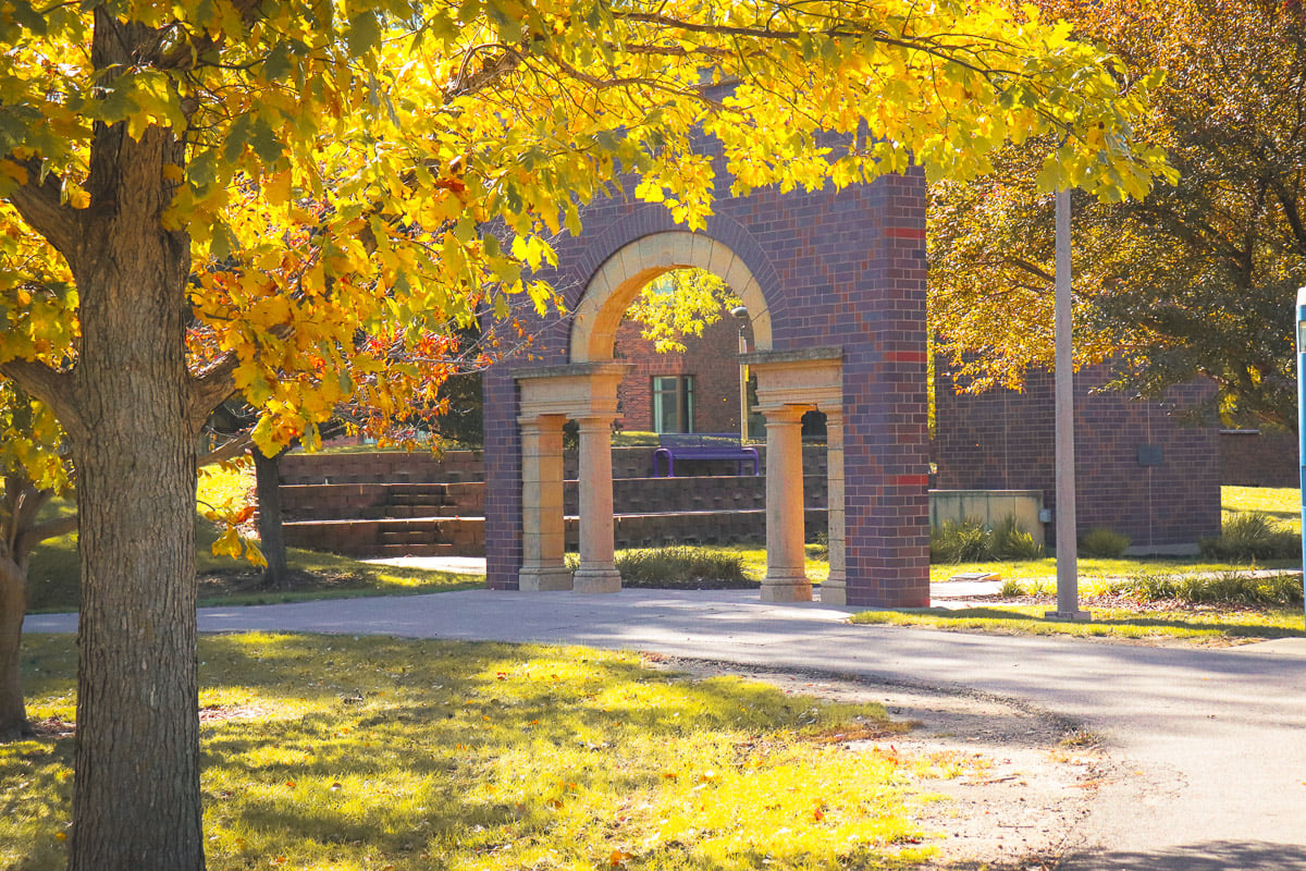 MSU Alumni Arch in late summer surrounded by trees with leaves starting to turn yellow.
