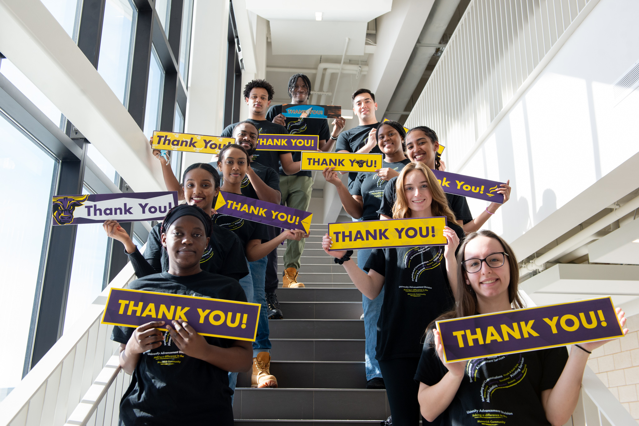 Group of students holding thank you signs, sitting on stairs. 
