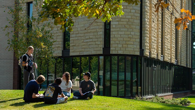 students sitting in a group outside on the lawn in front of the Clinical Sciences building. Fall leaves have begun to turn