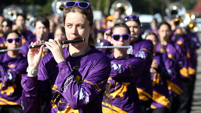 Homecoming marching band with all students in purple. Close up shot of a flute player as she marches in the Homecoming Parade.