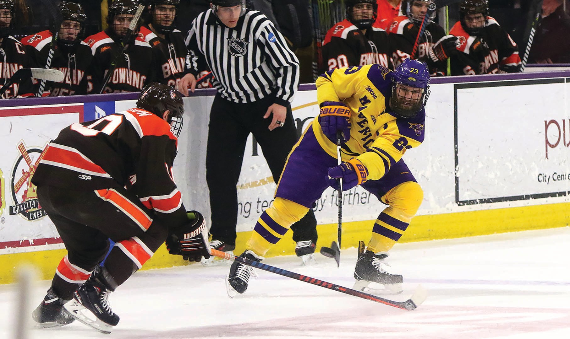 Maverick hockey player on the ice going after the puck against the other team with the referee in the background