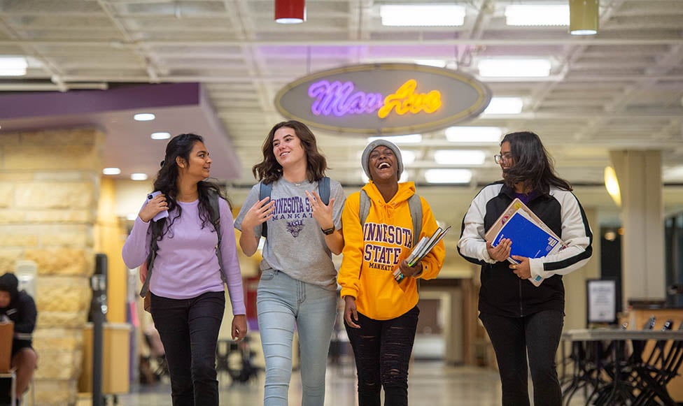 four students walking and laughing with the MavAve sign in the background