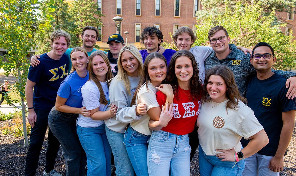 a group of students posing outside on campus all wearing their fraternity or sorority t-shirt
