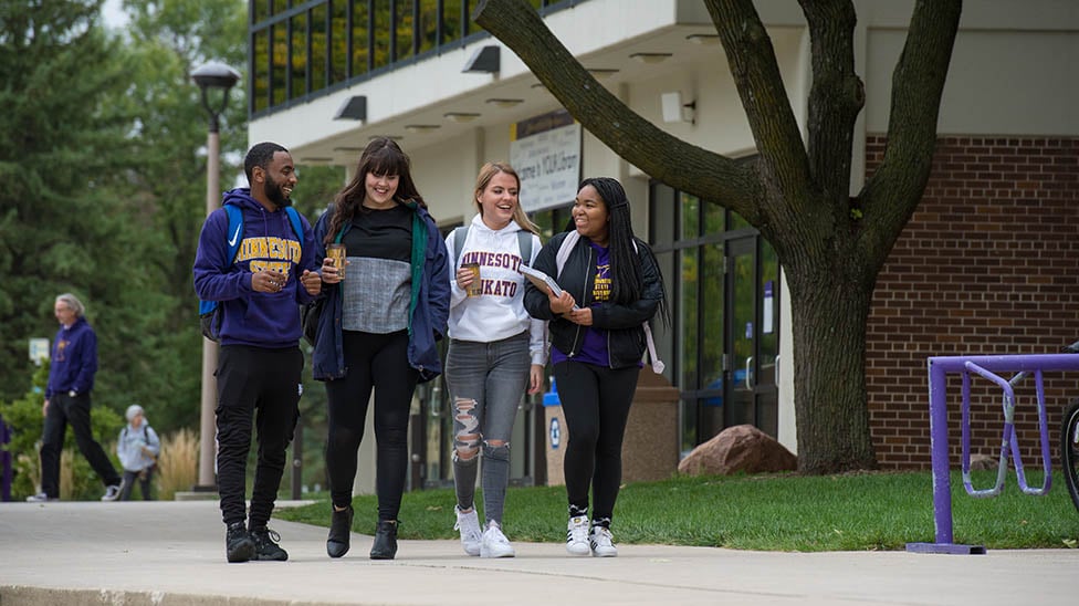 four students walking and talking on campus outside of the memorial library