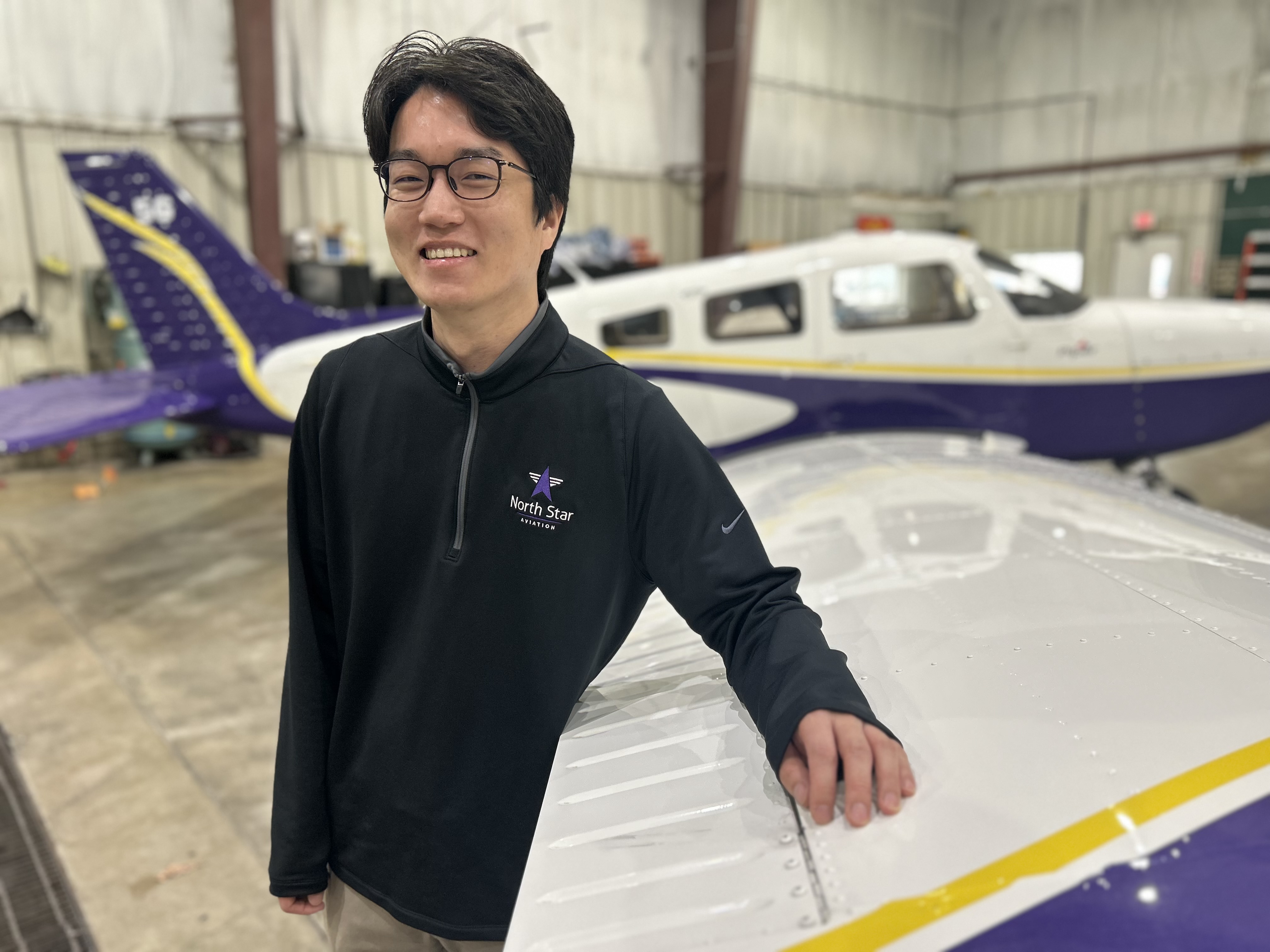 Sungjin Choi in leaning on an aircraft with additional MSU purple and gold planes in the background