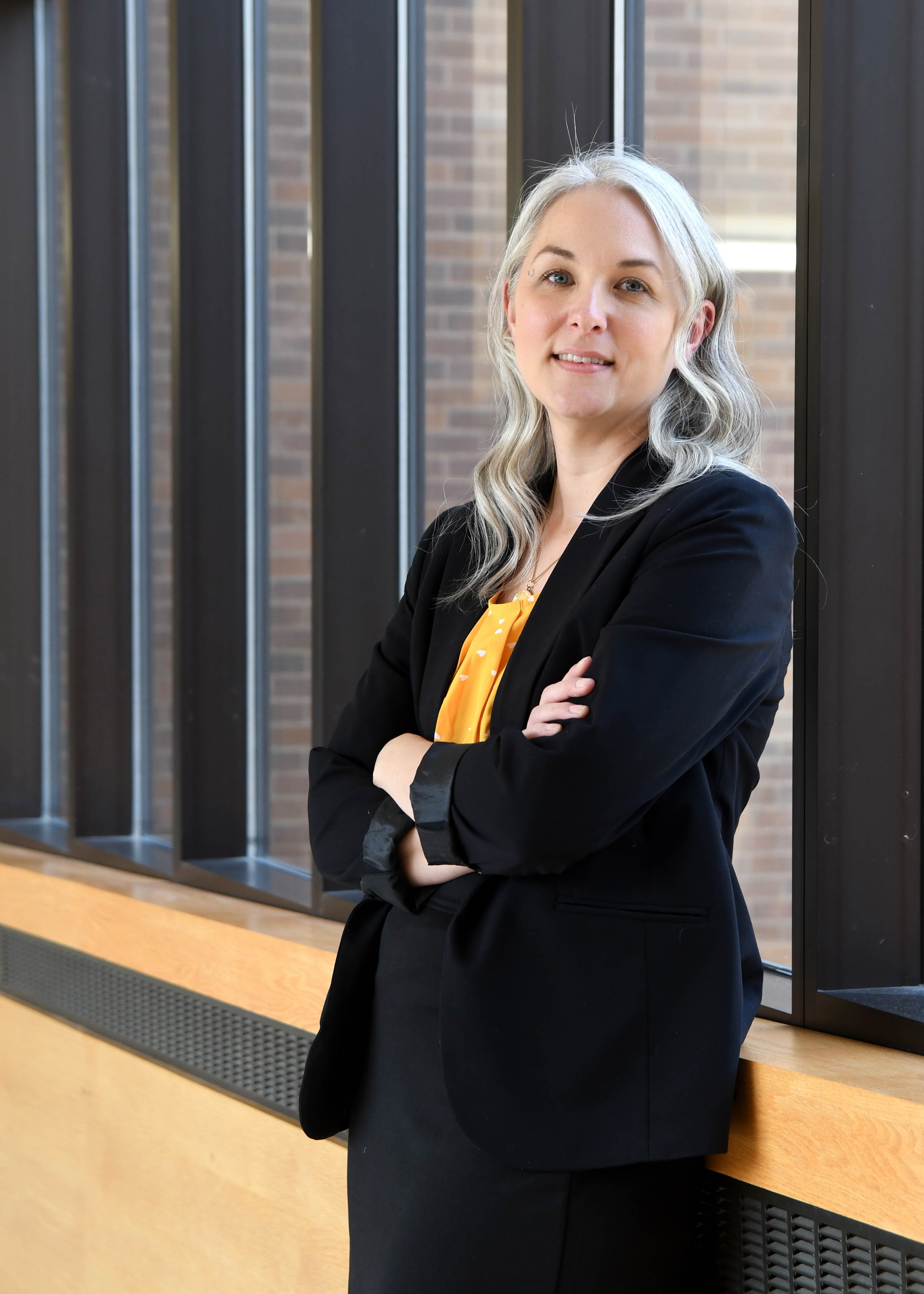 Katie Jolicoeur, director of career services in professional attire leaning against a window in the link between Morris Hall and Wigley admin building