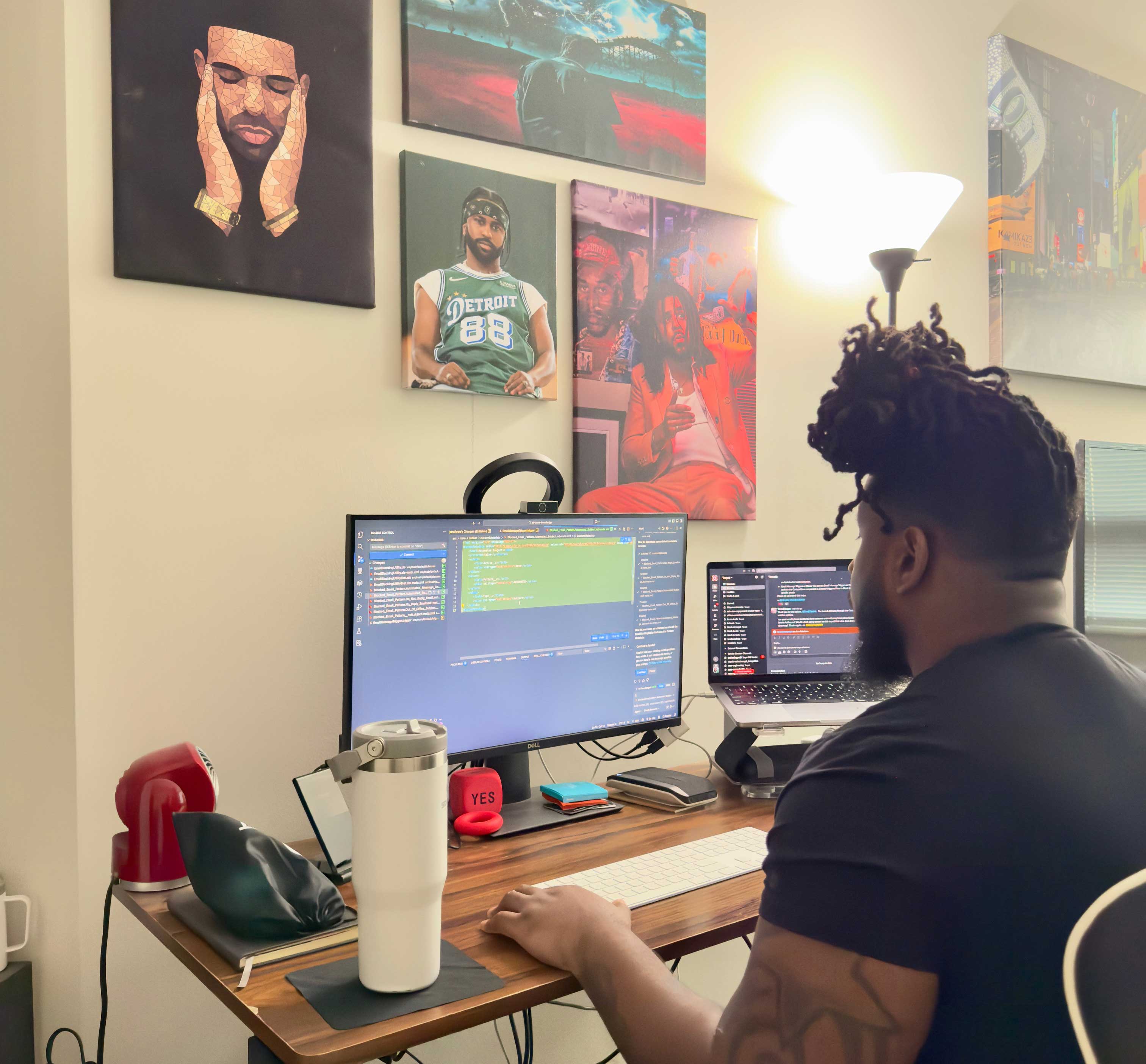 DAvon Goodwin sitting at his desk in his apartment working on his computer as a software engineer. His walls are filled with beautiful paintings