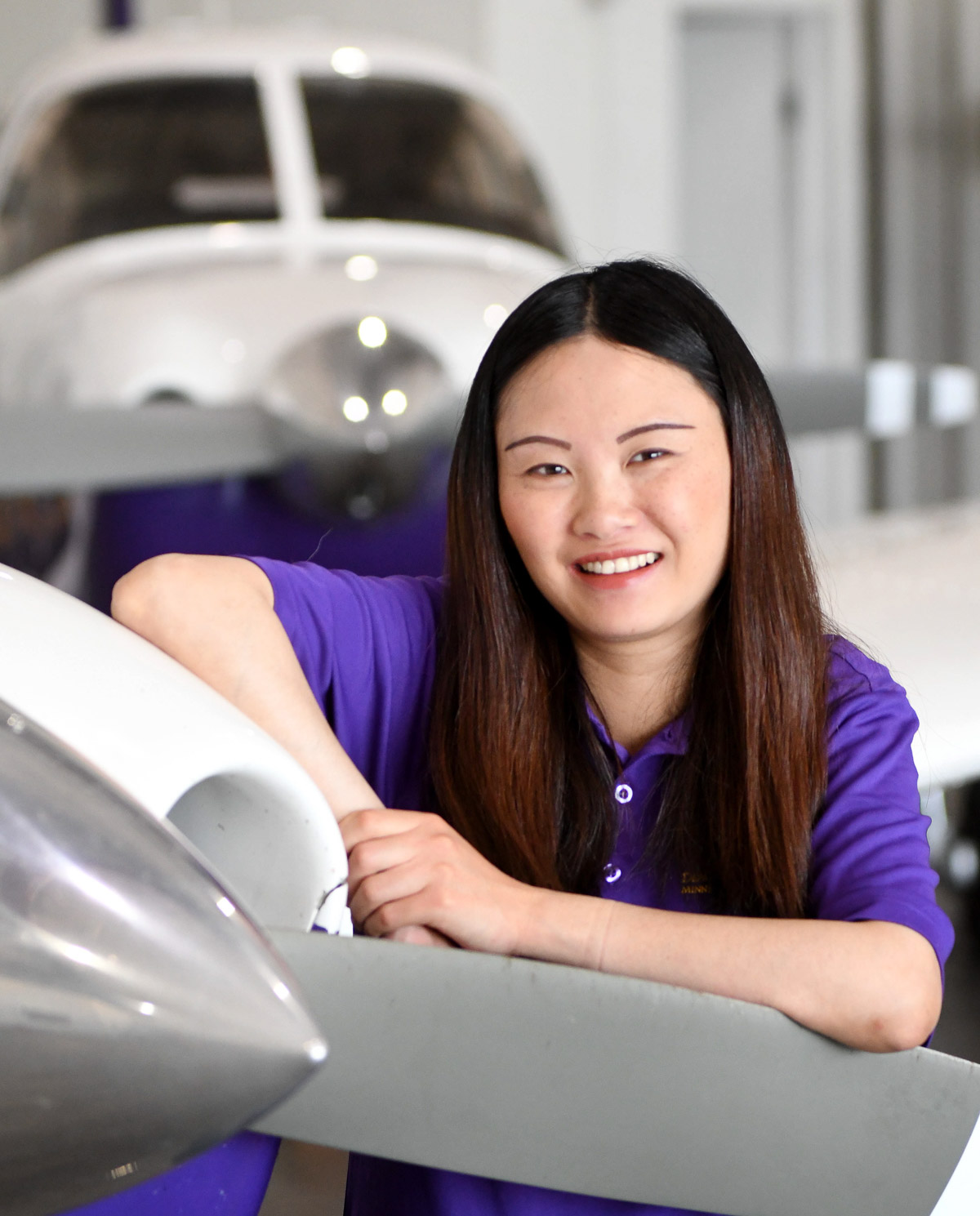 women with dark hair wearing a purple polo leaning on the wing of a plane 