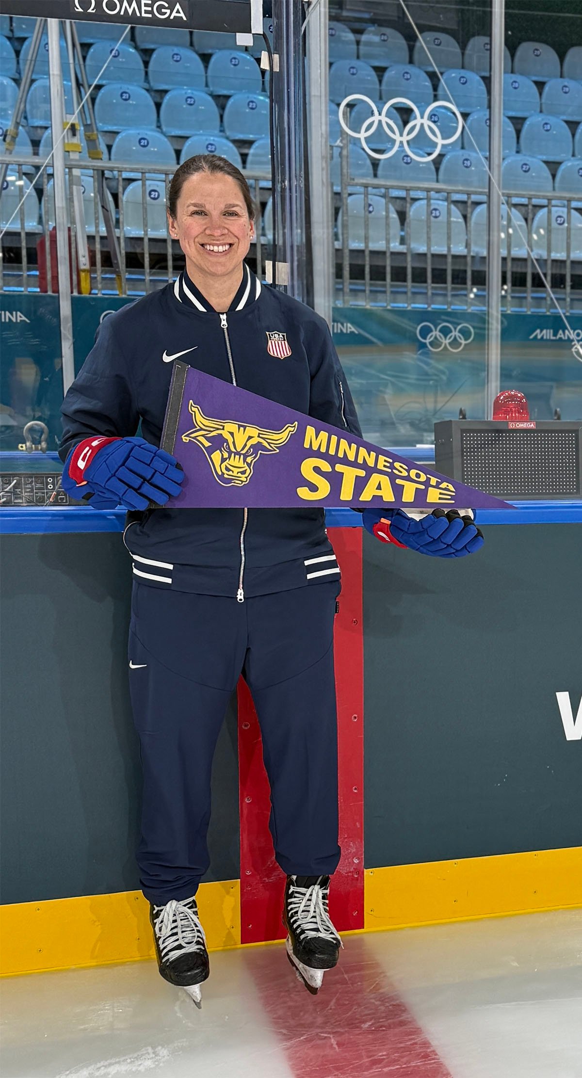 Shari Dickerman, former MSU women's hockey goalie, on the ice with skates on holding a MSU pennant.
