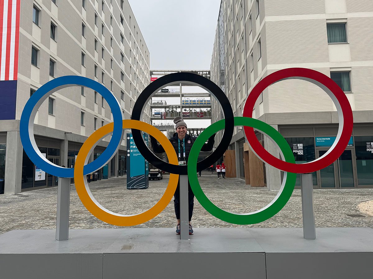 Shari Dickerman, former MSU women's goalie standing behind large Olympics sign in Italy.