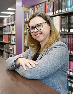 women with light brown hair and glasses, smiling with bookshelves in the background
