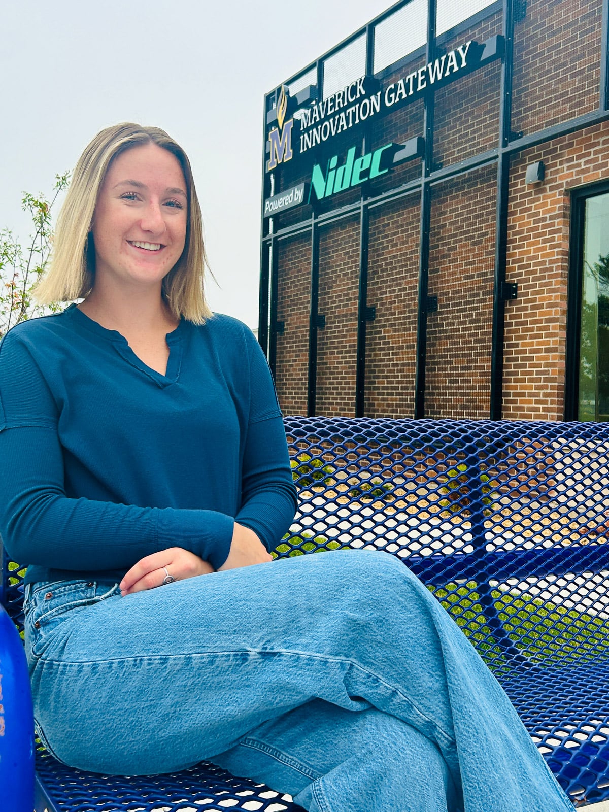 women with blonde hair and wearing casual attire sitting outside an office building on a purple bench