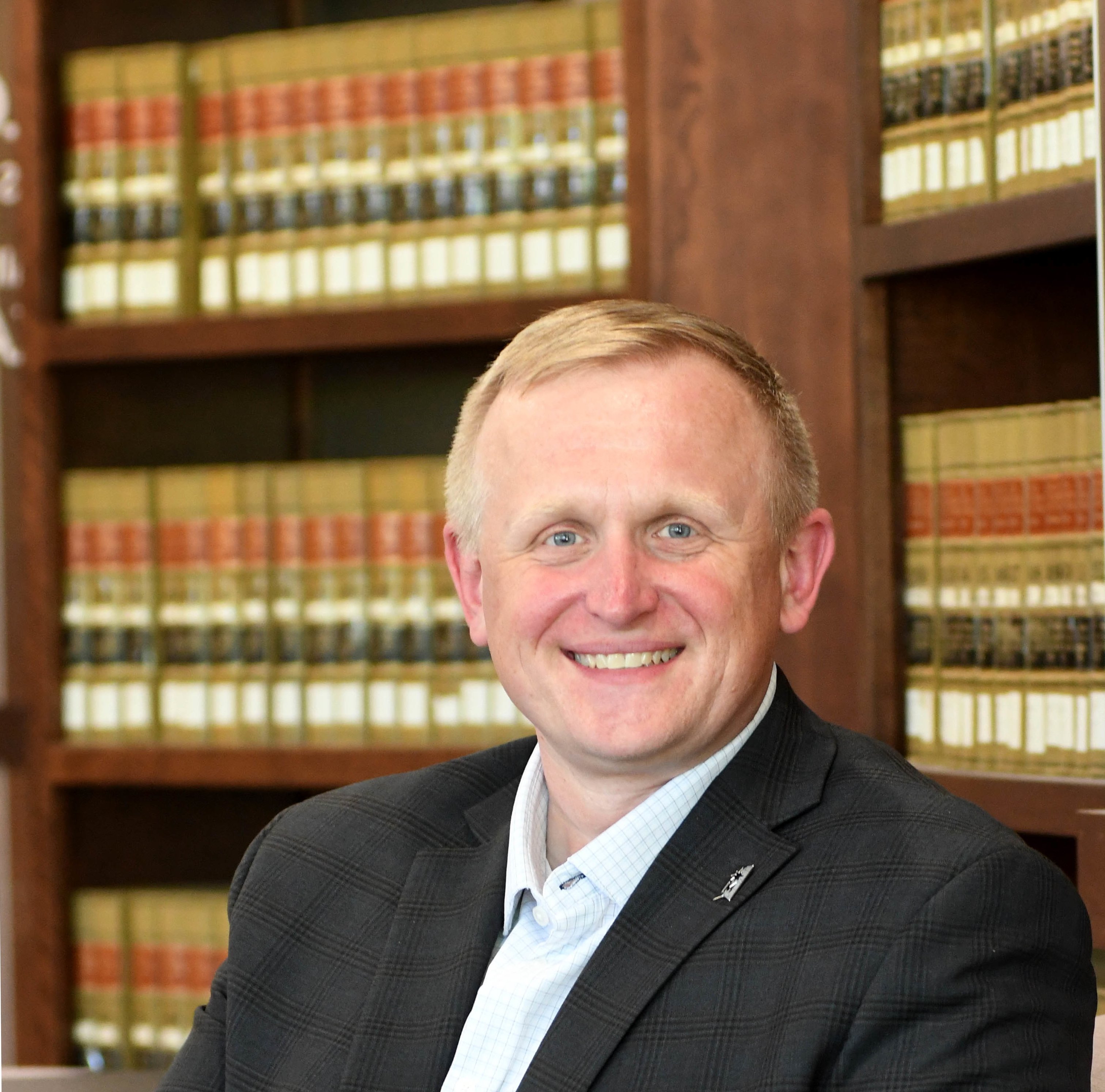 man sitting in chair in a business suit with bookshelves in the background