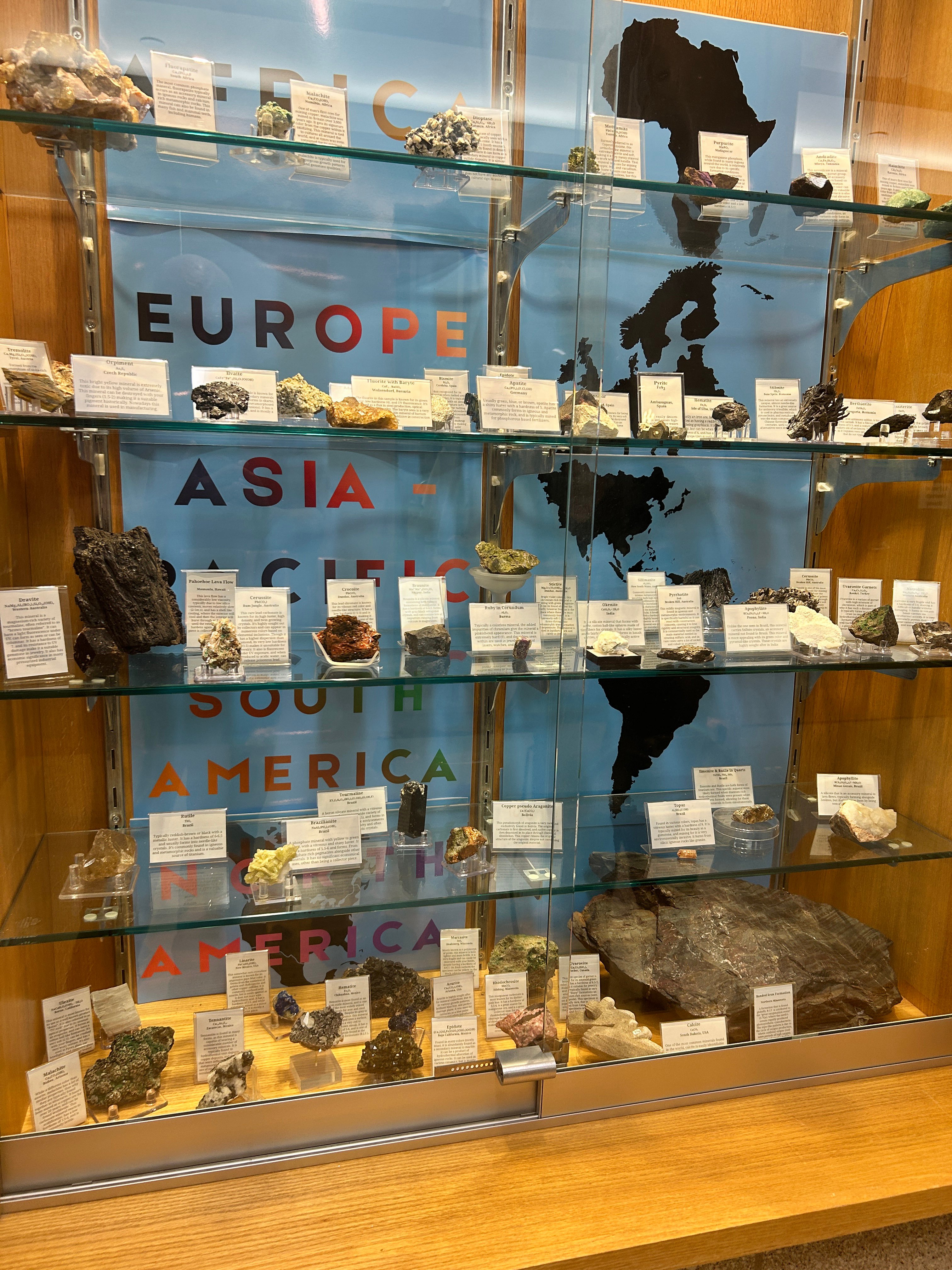 Glass showcase in an academic building showing the minerals, handwritten names and locations
