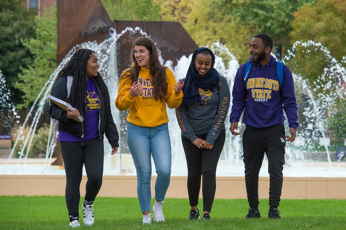 group of four students walking outside talking with the MSU fountain in the background