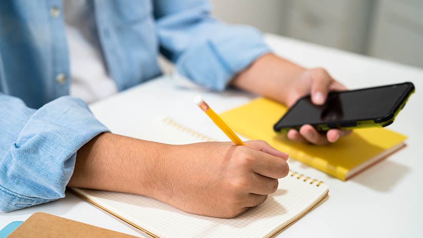 student with phone and notepad writing down information