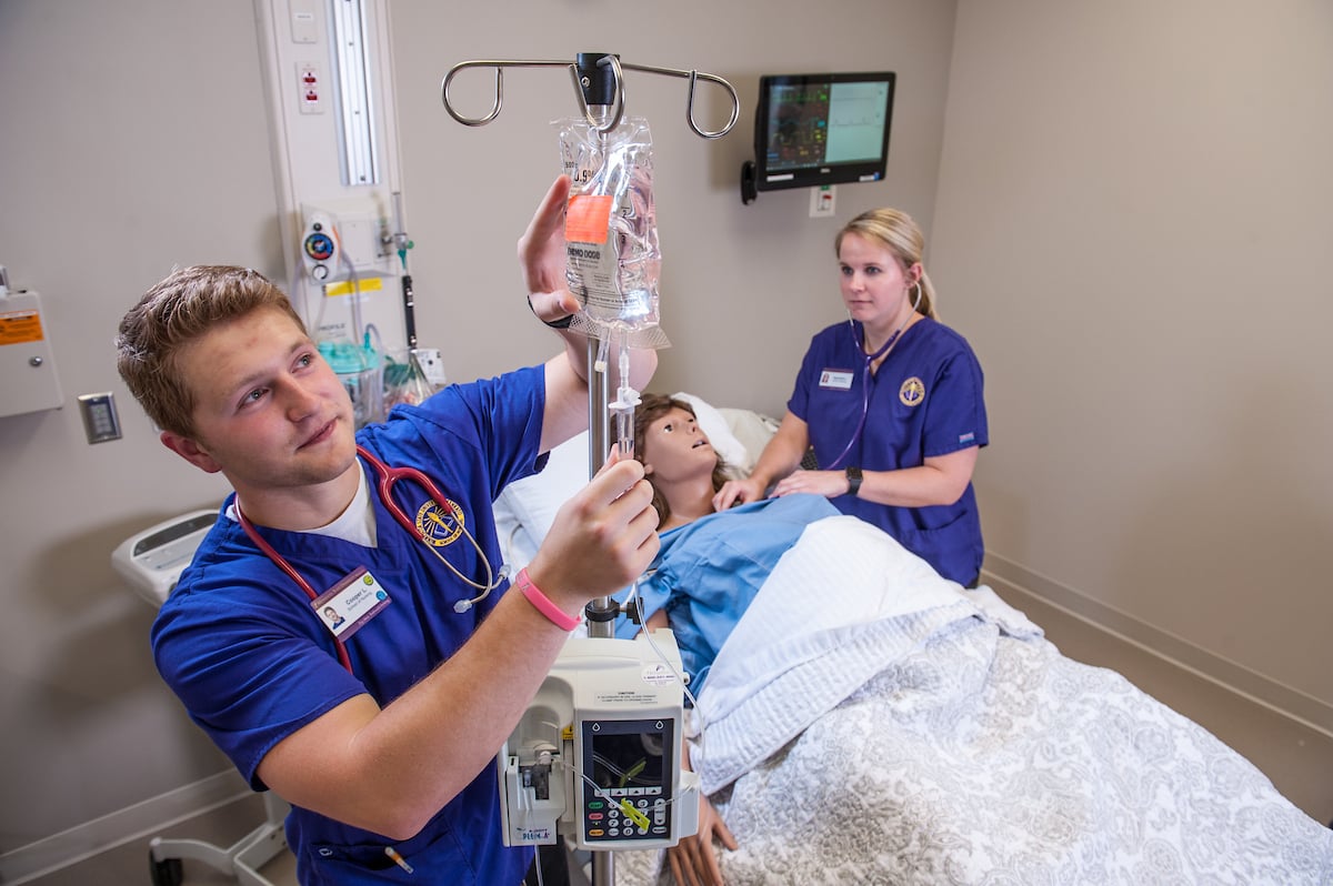 Nursing student checking IV bag in hospital environment.