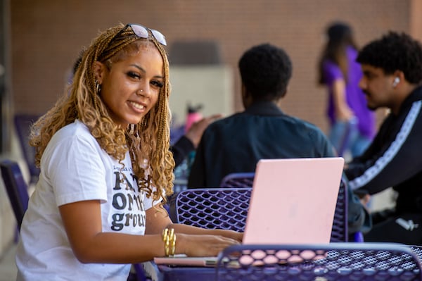Student sitting outside working on a computer, smiling. 