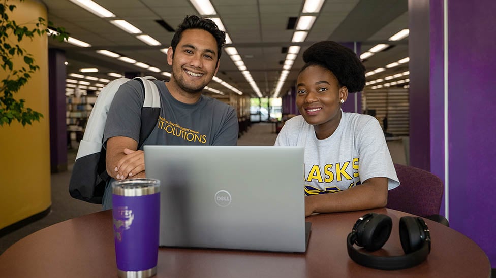 a person and person sitting at a table with a laptop