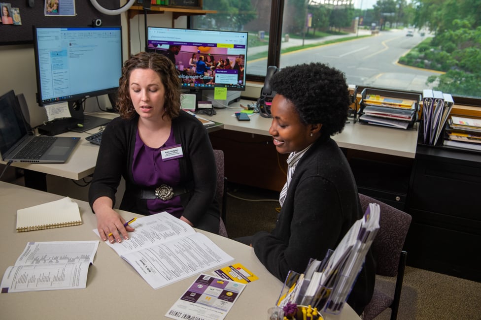 Student meeting with faculty in office talking and going over paperwork. 