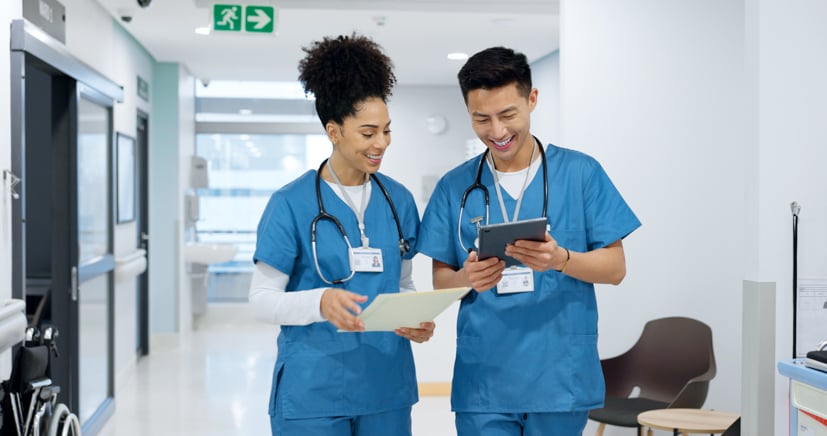 Two nurses walking through hallway talking to each other. 