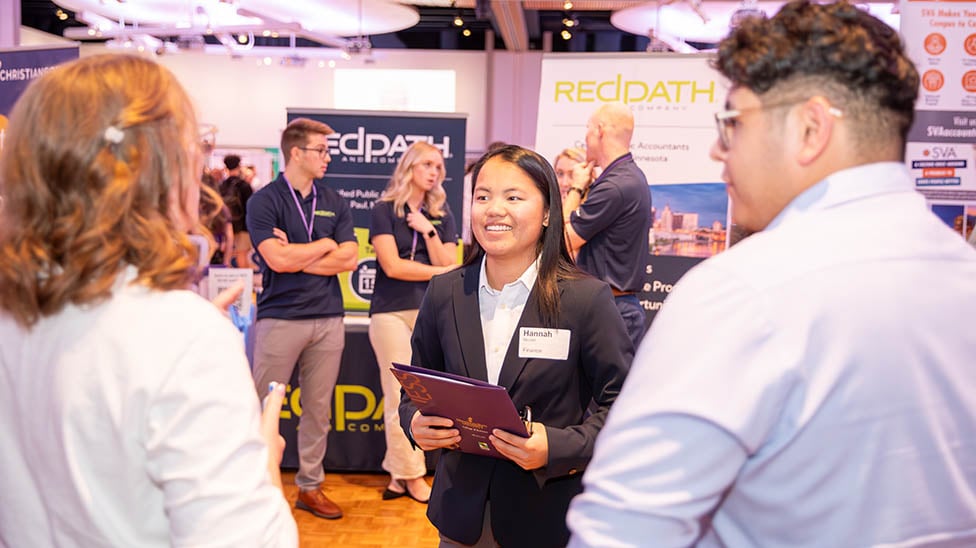 Image of a finance student speaking with two employers at a career fair