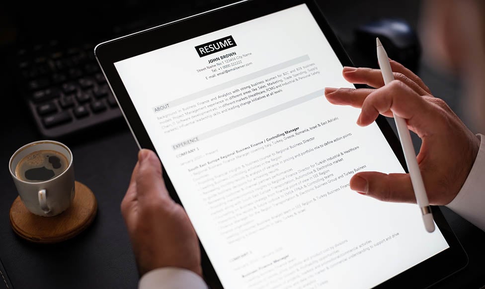 person working on their resume on an ipad with coffee nearby