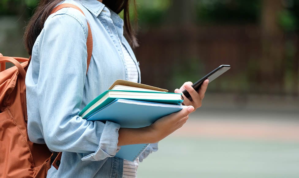 female student wearing her backpack and looking at her mobile phone while walking on campus