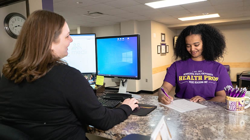 student filling out paperwork at a front desk in the student health services office on campus