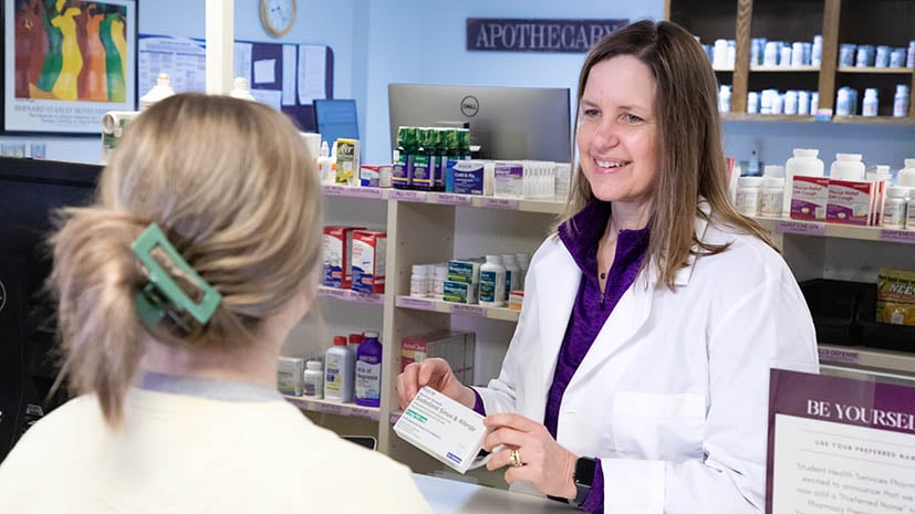 pharmacist showing a student some medication with the pharmacy in the background