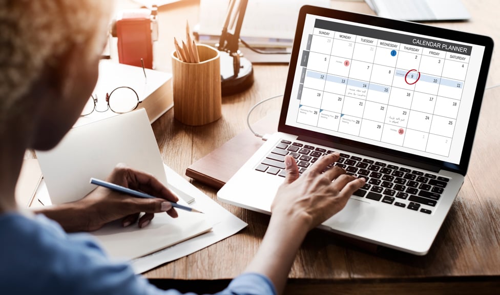 Women sitting in front of a computer with a calendar up on the screen. 