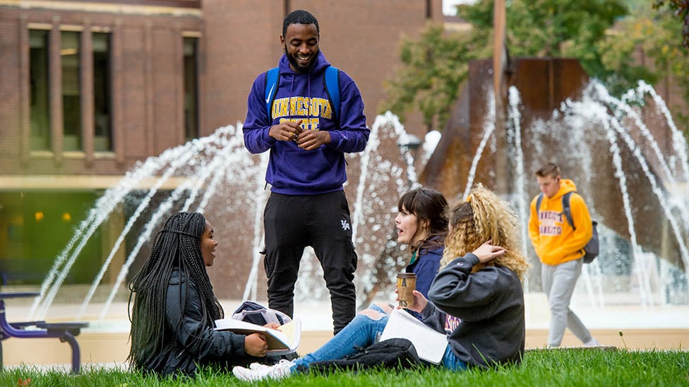 four students hanging out around the fountain near the CSU. Talking and studying together