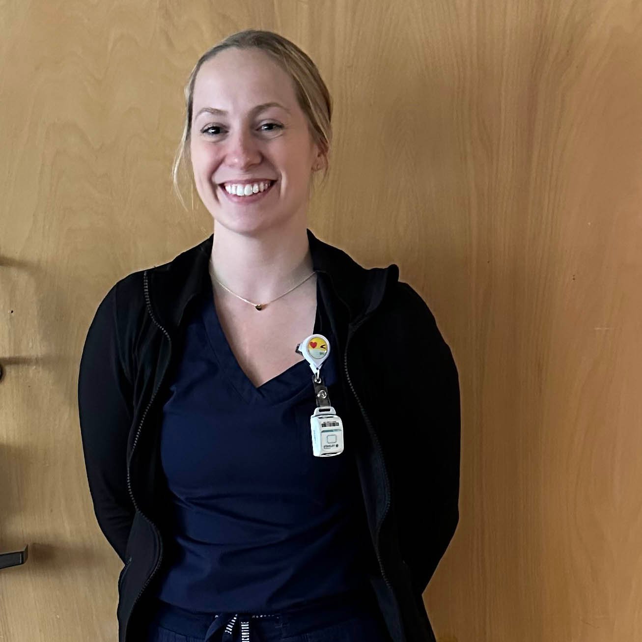 Nurse and alum, Madison Marien, stands in her scrubs in front of a clinic door