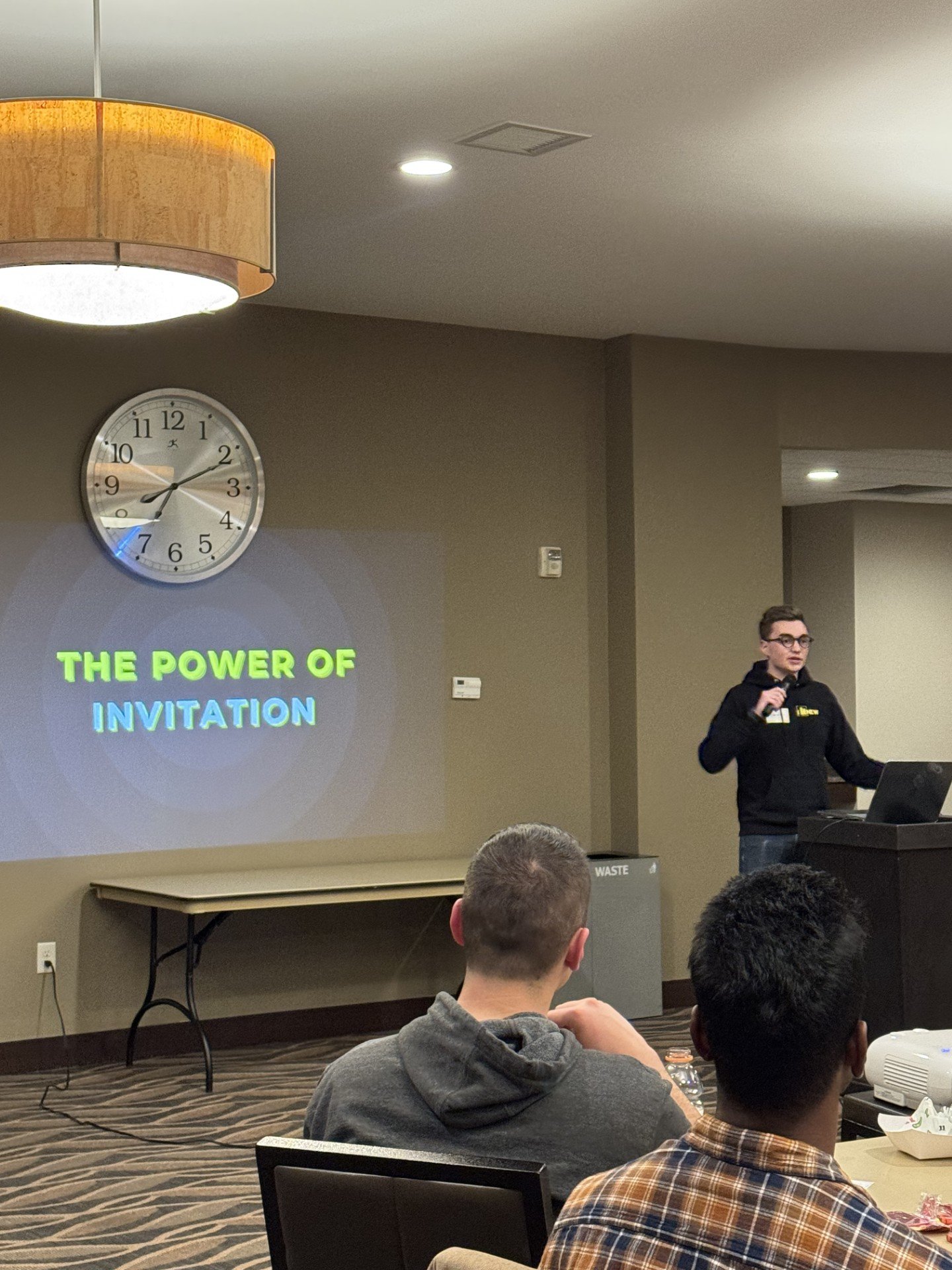 Jackson presenting at NEW Minneapolis with the powerpoint screen reading the power of invitation.