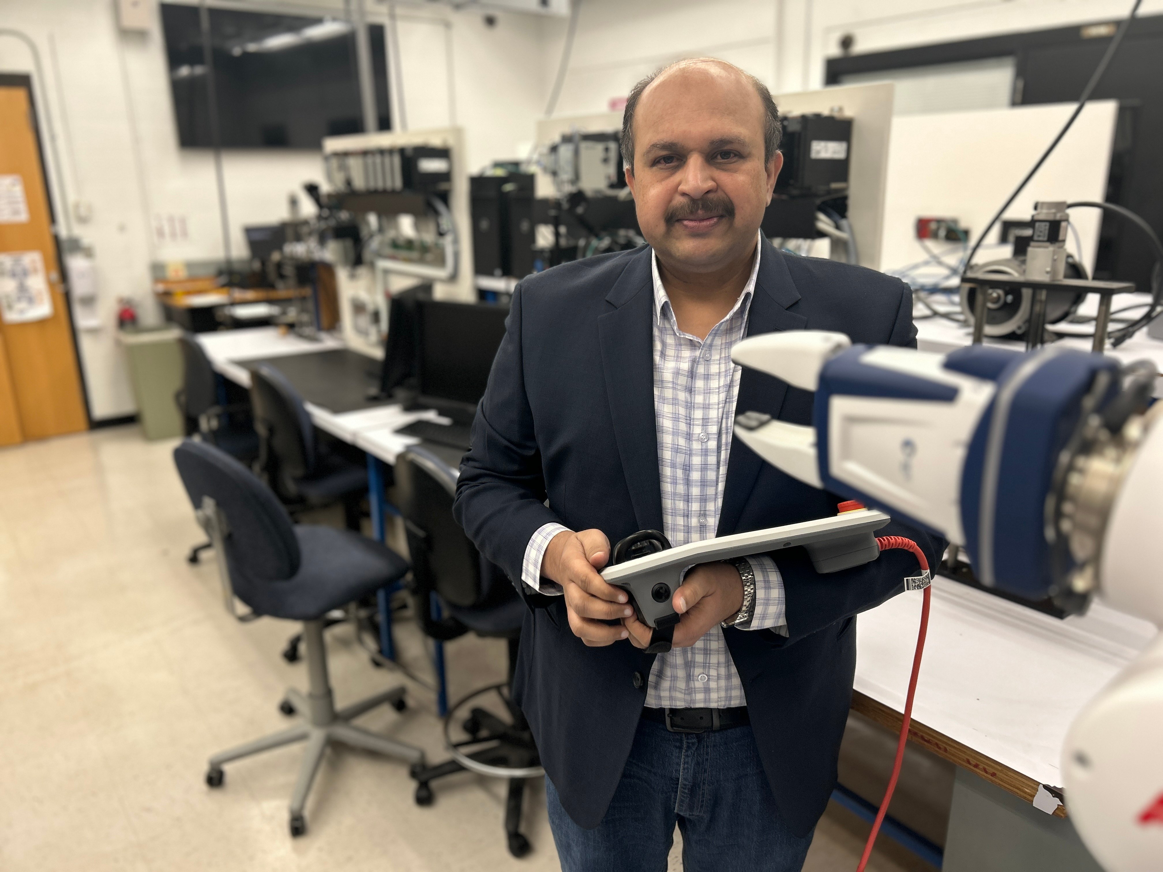 Dr. Dharmadhikari in the lab smiling at the camera while holding a piece of equipment.