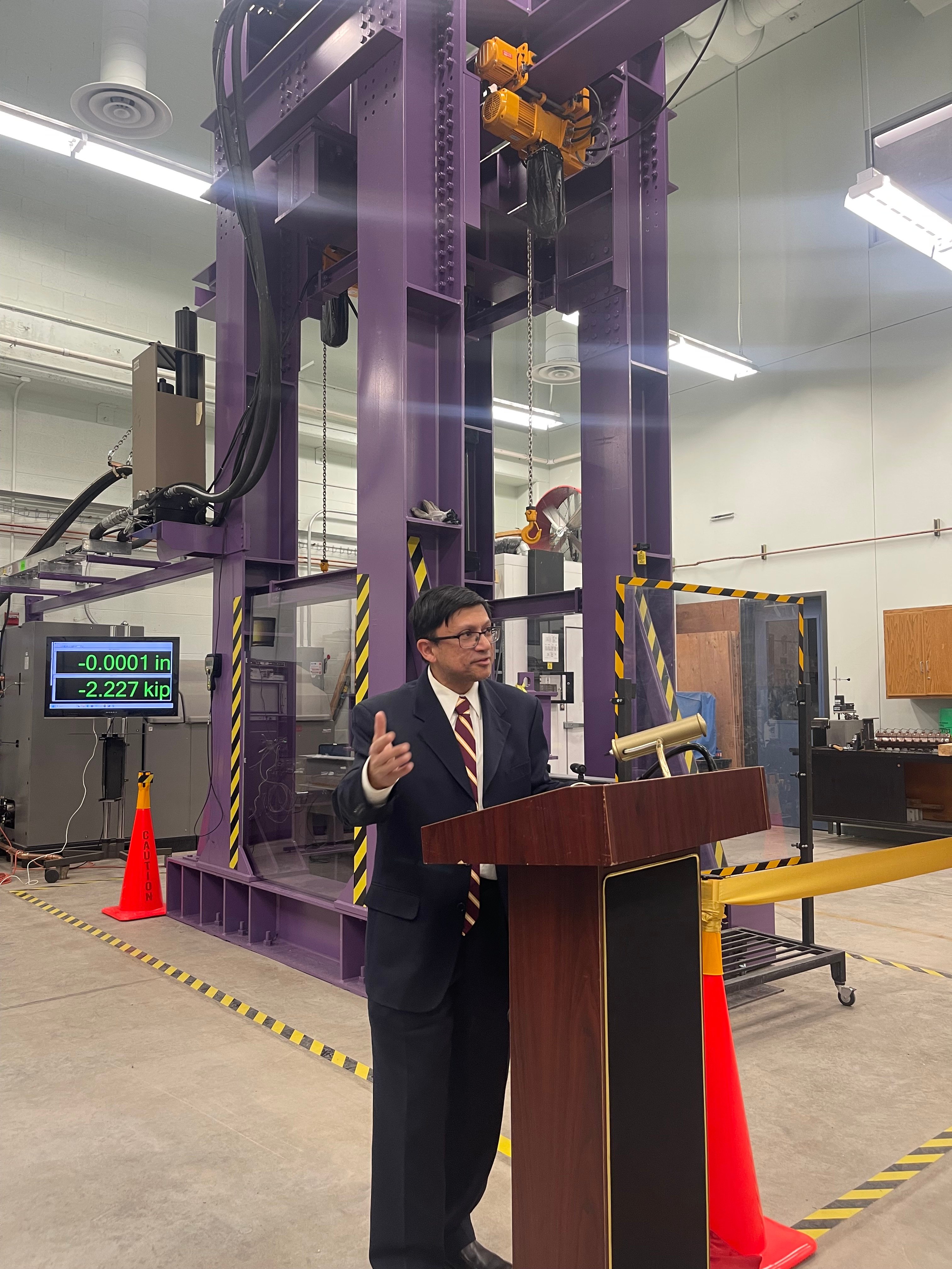 Professor Fahad Reza presenting at a podium with the force load machine behind him