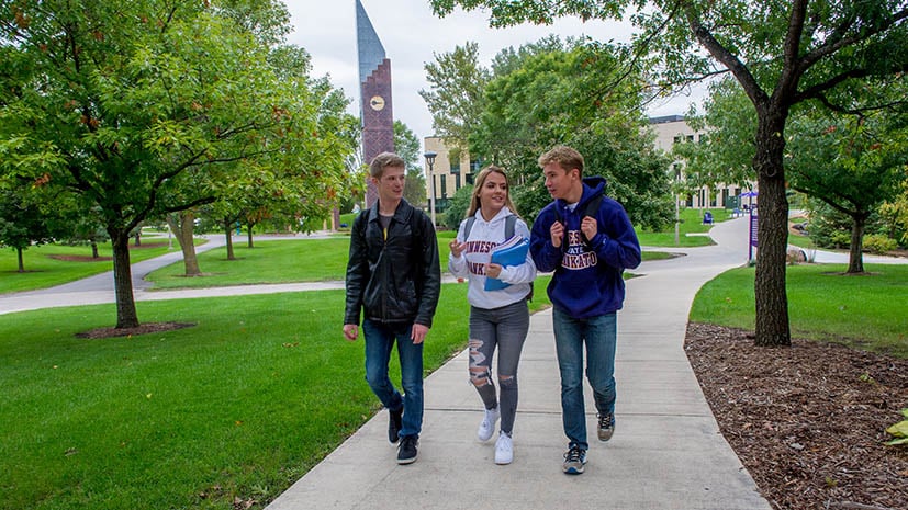 three students walking on campus in front of the clock tower
